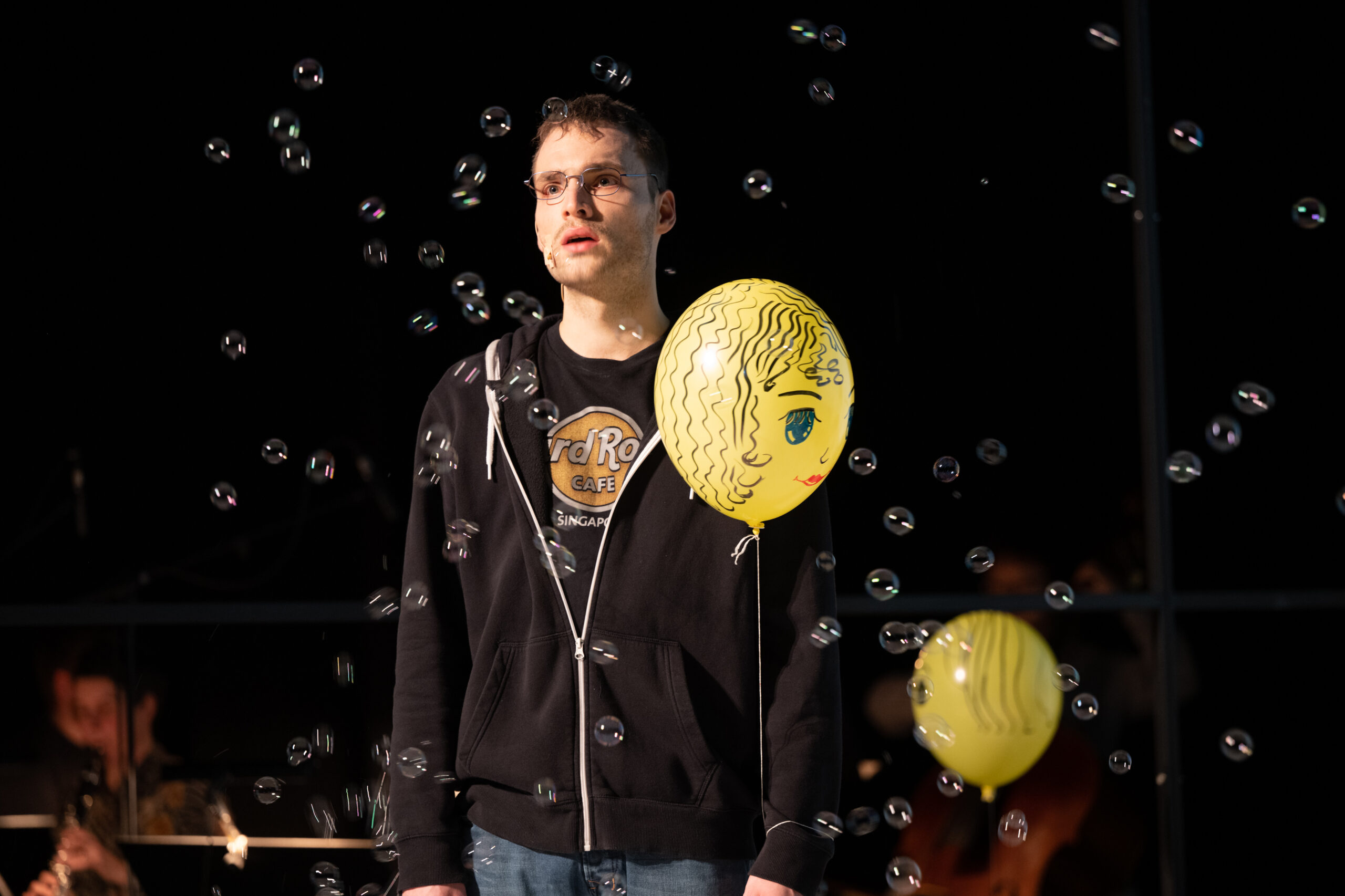 Freak mit Brille und Luftballon weint, um ihn herum Seifenblasen in der Luft
